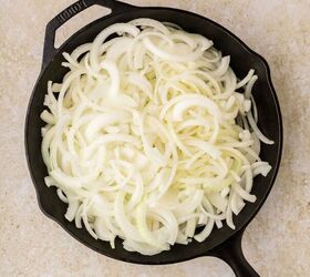 french onion pasta, A cast iron skillet filled with raw thinly sliced yellow onions sits on a light beige countertop