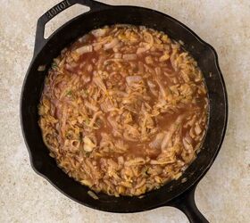 french onion pasta, A cast iron skillet filled with caramelized onions simmering in a brown brothy liquid placed on a light beige countertop