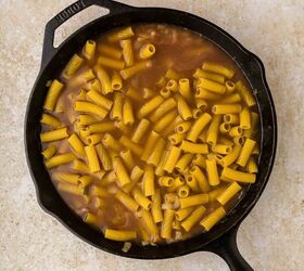 french onion pasta, A black cast iron skillet filled with uncooked rigatoni pasta and brown liquid set on a light beige countertop
