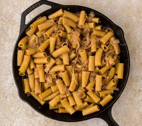 french onion pasta, A black cast iron skillet filled with cooked rigatoni pasta mixed with caramelized onions set on a light beige textured surface