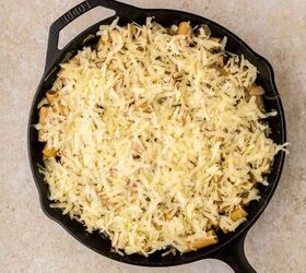 french onion pasta, A black cast iron skillet filled with shredded cheese covering a layer of cooked ingredients set on a light colored countertop