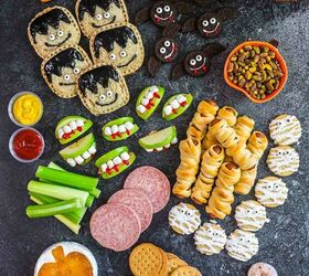 spooky sweet the ultimate halloween charcuterie board, A Halloween themed snack platter with treats shaped like mummies monsters and vampires apple slices with candy teeth crackers pretzels dipping sauces pistachios cookies and donuts surrounded by two pumpkins