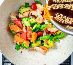homemade shrimp and vegetable stir fry in 30 minutes, Pouring sesame soy stir fry sauce over shrimp and vegetables in a wok