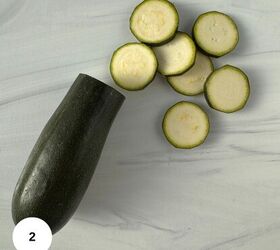 mediterranean roasted zucchini slices, A whole zucchini with several roasted zucchini slices arranged on a light gray marble surface A white circle with the number 2 is in the bottom left corner