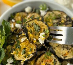 mediterranean roasted zucchini slices, A fork holds a slice of roasted zucchini garnished with herbs crumbled feta cheese and lemon zest above a bowl brimming with roasted zucchini slices and fresh herbs