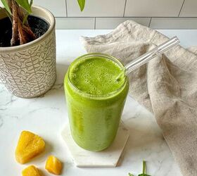 detox island green smoothie tropical smoothie cafe copycat, A green tropical smoothie in a glass with a clear straw on a countertop with fruit and spinach next to the glass