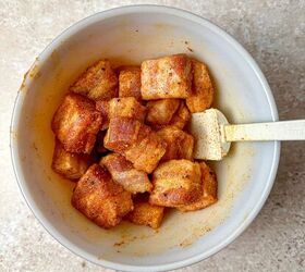 air fryer pork belly crispy bites, A spoon in a mixing bowl with seasoned pork belly cubes