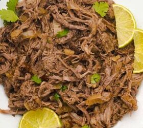 loaded baked potato with brisket, Shredded oven braised beef barbacoa that has been cooked in a Dutch oven is on a white plate