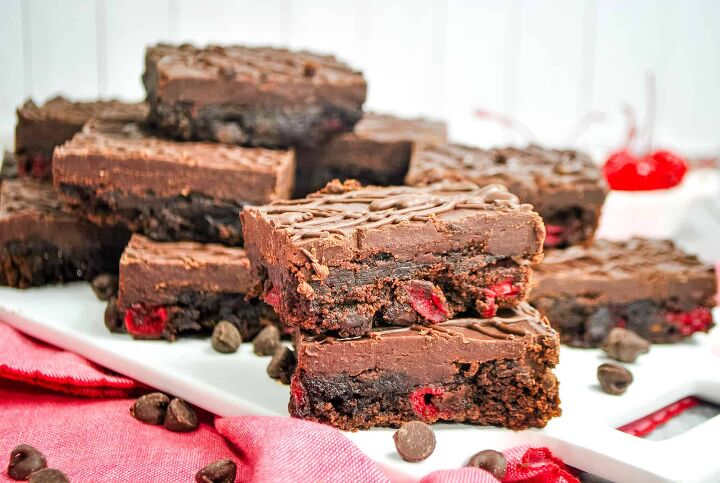 cherry brownies, cherry brownies topped with chocolate ganache on a platter with chocolate chips scattered around
