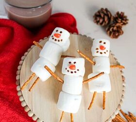 cute and easy marshmallow snowmen for the holidays, Cute marshmallow snowmen on a wooden stand surrounded by pretzel sticks marshmallows and a cup of hot chocolate