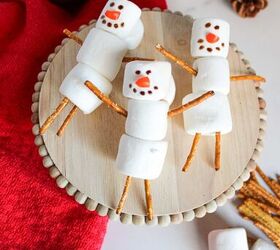 cute and easy marshmallow snowmen for the holidays, Marshmallow snowmen on a wooden stand surrounded by pretzel sticks marshmallows and a cup of hot chocolate
