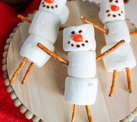 cute and easy marshmallow snowmen for the holidays, Top view of marshmallow snowmen with pretzel arms and legs festive towel and hot chocolate in the background