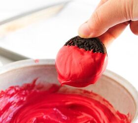 easy christmas oreos santa s toy bag oreos recipe, A hand dipping a chocolate sandwich cookie halfway into melted red candy coating