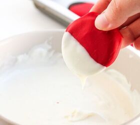 easy christmas oreos santa s toy bag oreos recipe, A hand dipping the red coated cookie into melted white chocolate to create a layered effect