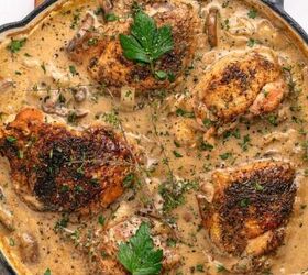 easy chicken roulade recipe with spinach sundried tomatoes gf, A skillet filled with four browned chicken thighs in a creamy mushroom sauce inspired by Chicken Marsala garnished with fresh parsley and herbs sits on a wooden board with a small dish of ground pepper nearby