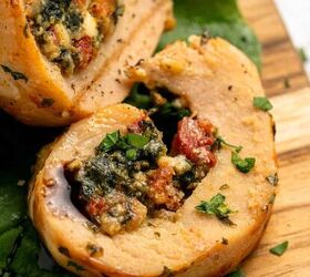 easy chicken roulade recipe with spinach sundried tomatoes gf, Close up of two slices of chicken roulade filled with spinach sundried tomatoes and cheese garnished with chopped herbs and served on a wooden board with fresh green leaves underneath