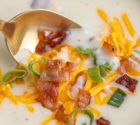 loaded potato soup, A close up of creamy potato soup in a white bowl topped with shredded cheddar cheese crispy bacon pieces and sliced green onions A gold spoon is resting in the soup