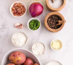 loaded potato soup, An assortment of loaded potato soup ingredients on a white marble surface including red potatoes shredded cheese chicken broth bacon red onion garlic green onions sour cream flour butter milk salt and pepper