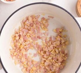 loaded potato soup, Chopped red onion and garlic cooking in a white pot viewed from above Surrounding the pot are small bowls containing cooked bacon pieces and sliced green onions on a marble countertop
