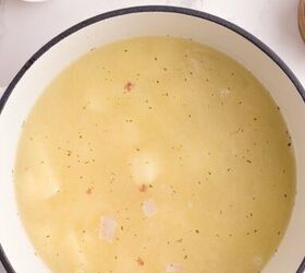 loaded potato soup, A pot of light colored soup with visible potato chunks sits on a white surface Nearby small bowls hold chopped bacon and sliced green onions