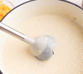 loaded potato soup, A large pot filled with creamy light colored soup with an immersion blender partially submerged Ingredients like shredded cheese and chopped green onions are visible in small bowls nearby