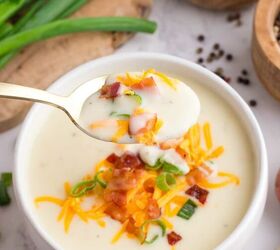 loaded potato soup, A bowl of creamy potato soup topped with shredded cheese chopped green onions and bacon pieces A spoonful of the soup is held above the bowl ready to eat Green onions and seasonings are nearby