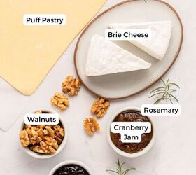 cranberry brie puff pastry bites gluten free, A flat lay for Cranberry Brie Puff Pastry Bites labeled ingredients on a white surface include a sheet of puff pastry brie wedges on a plate bowls of walnuts and cranberry jam and sprigs of rosemary