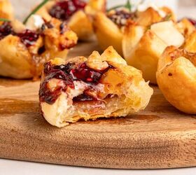 cranberry brie puff pastry bites gluten free, Close up of flaky Puff Pastry Bites filled with melted brie cheese and cranberry jam garnished with nuts on a wooden board One cup in the foreground has a bite taken out revealing the creamy filling inside