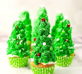 easy christmas tree cupcakes to brighten holidays, Front view of multiple Christmas tree cupcakes with green frosting candy ornaments and powdered sugar snow arranged on a marble surface