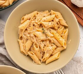 french onion pasta with gruyere cheese, A beige bowl filled with creamy French Onion Pasta topped with shredded Gruy re cheese black pepper and a sprig of thyme A fork a gray napkin and fresh garlic are nearby