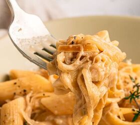 french onion pasta with gruyere cheese, Close up of a fork holding creamy French Onion Pasta with penne and fettuccine coated in a rich Gruy re sauce The dish is garnished with black pepper and herbs in a beige bowl