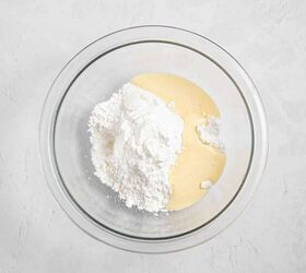 best eggnog pound cake rum eggnog glaze, A glass mixing bowl containing a mound of white powdered sugar and a pool of pale yellow liquid set on a light textured surface