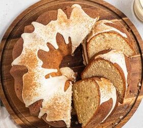 best eggnog pound cake rum eggnog glaze, A sliced eggnog pound cake with white icing and a sprinkle of cinnamon sits on a round wooden board with a few slices cut and separated Forks and glasses of creamy drinks are nearby on a light striped cloth