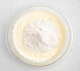 best eggnog pound cake rum eggnog glaze, A glass bowl containing a creamy yellow batter with a mound of white flour on top ready to be mixed sits on a light textured surface