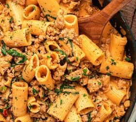 creamy italian sausage pasta with spinach, A close up of creamy pasta with Italian sausage in a rich sauce fresh herbs and rigatoni stirred together in a skillet with a wooden spoon