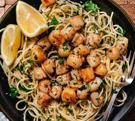 sauteed bay scallops, seared bay scallops served over spaghetti with parsley and lemon wedges on a black plate