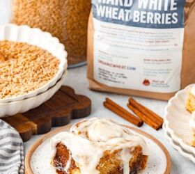 cinnamon rolls with fresh milled flour, Frosted cinnamon roll on plate in front with wheat berries labeled bag and cinnamon sticks nearby