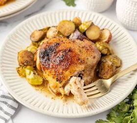 sheet pan chicken thighs, Baked chicken thigh with roasted brussels sprouts and potatoes on a plate with a fork holding a piece of the chicken thigh cut open