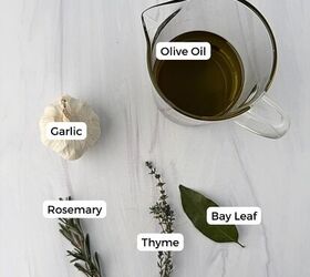 garlic confit with thyme and rosemary, A glass measuring cup of olive oil a head of garlic a sprig of rosemary thyme and a bay leaf are arranged on a white surface perfect ingredients for homemade garlic confit Each item is labeled with text