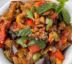 garlic confit with thyme and rosemary, A white bowl filled with colorful Sicilian caponata featuring chunks of eggplant tomatoes bell peppers and herbs garnished with fresh mint leaves A spoon rests in the bowl on a light surface