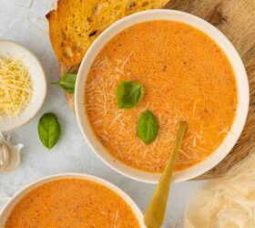 roasted red pepper and tomato soup, Two bowls of creamy red pepper and tomato soup topped with grated cheese and fresh basil leaves served with slices of toasted bread on a wooden board A small bowl of shredded cheese and a clove of garlic are nearby