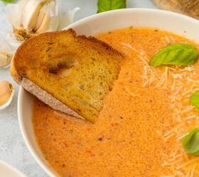 roasted red pepper and tomato soup, A bowl of creamy red pepper and tomato soup topped with shredded cheese and fresh basil leaves served with a slice of toasted bread Garlic bulbs and more cheese are visible in the background
