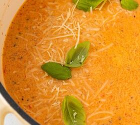roasted red pepper and tomato soup, A creamy orange soup garnished with fresh basil leaves and shredded Parmesan cheese served in a white pot The soup surface shows flecks of herbs and a smooth rich texture
