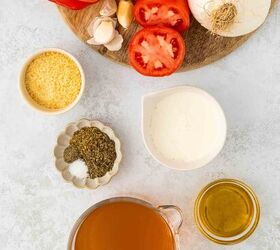roasted red pepper and tomato soup, Ingredients for red pepper and tomato soup arranged on a white surface fresh tomatoes onion garlic grated cheese dried herbs and salt cream olive oil and a measuring cup of vegetable broth
