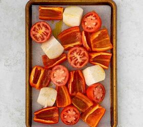 roasted red pepper and tomato soup, A baking tray with parchment paper holds chopped red bell peppers halved tomatoes and large chunks of onion all drizzled with oil and sprinkled with pepper ready to be roasted