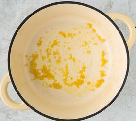 roasted red pepper and tomato soup, A large cream colored pot with two handles contains a small amount of oil and garlic spread across the bottom The pot is placed on a light gray textured surface