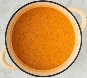roasted red pepper and tomato soup, A large cream colored pot filled with creamy orange colored soup or sauce speckled with herbs and spices sits on a light gray surface