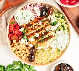 mediterranean chicken couscous bowl, A Mediterranean bowl filled with grilled chicken couscous cherry tomatoes chickpeas cucumber kalamata olives red onion tzatziki sauce and crumbled feta cheese surrounded by bowls of olives and tomatoes