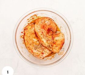 mediterranean chicken couscous bowl, Raw seasoned chicken breasts marinating in spices and oil inside a clear glass bowl ready to become Mediterranean Chicken Couscous The bowl sits on a white surface with a white circle and the number 1 in the lower left corner