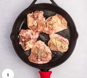 creamy chicken orzo bake one pan dinner, Five raw seasoned chicken thighs arranged in a cast iron skillet with a red handle ready to become part of a delicious chicken orzo bake Set on a light gray surface a white circle with the number 1 appears in the lower left corner